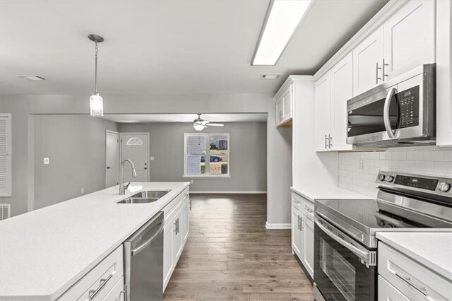 kitchen featuring appliances with stainless steel finishes, sink, wood-type flooring, white cabinetry, and pendant lighting