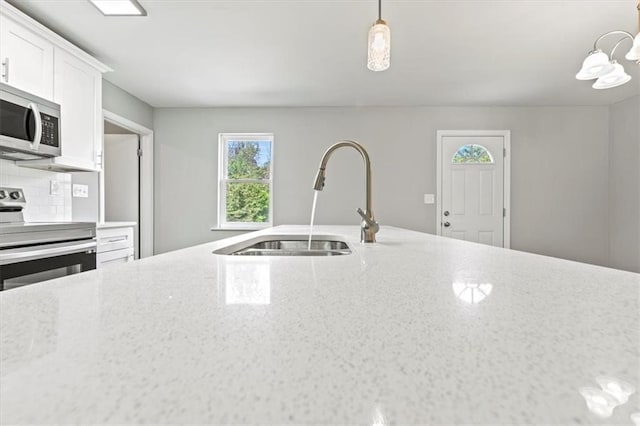 kitchen with sink, white cabinetry, stainless steel appliances, pendant lighting, and light stone counters