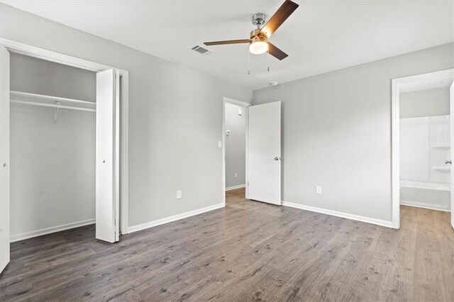 unfurnished bedroom with a closet, ceiling fan, wood-type flooring, and ensuite bath