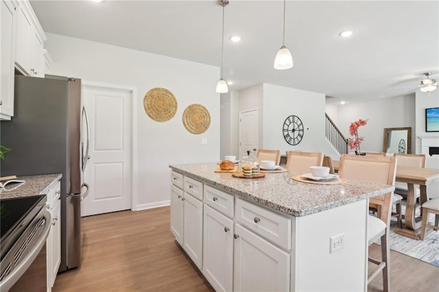 11113 Suria Dr, Covington, GA 30014 - kitchen featuring stainless steel range with electric cooktop, a breakfast bar area, light wood-style floors, white cabinets, and a kitchen island
