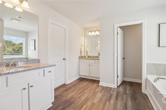 11113 Suria Dr, Covington, GA 30014 - full bathroom with two vanities, wood finished floors, a garden tub, and a chandelier