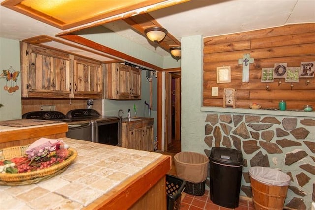 kitchen with washer and dryer, brown cabinets, a sink, tile countertops, and rustic walls