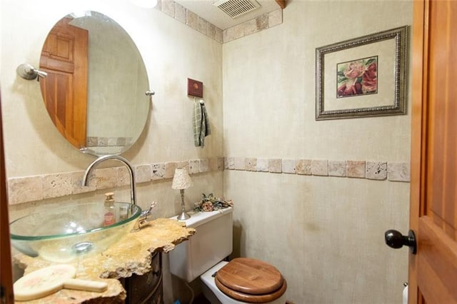 half bath with visible vents, tile walls, toilet, and vanity