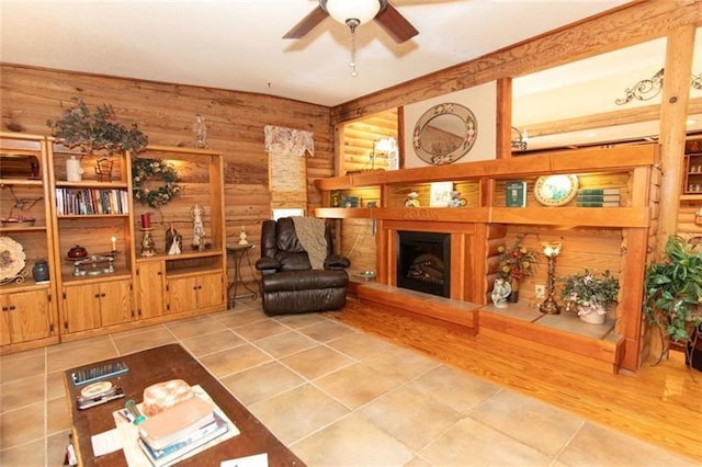 living area featuring tile patterned floors, rustic walls, a ceiling fan, and a fireplace with raised hearth