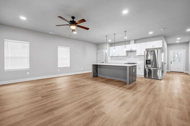 kitchen featuring stainless steel fridge, white cabinetry, hanging light fixtures, a kitchen island with sink, and a kitchen bar