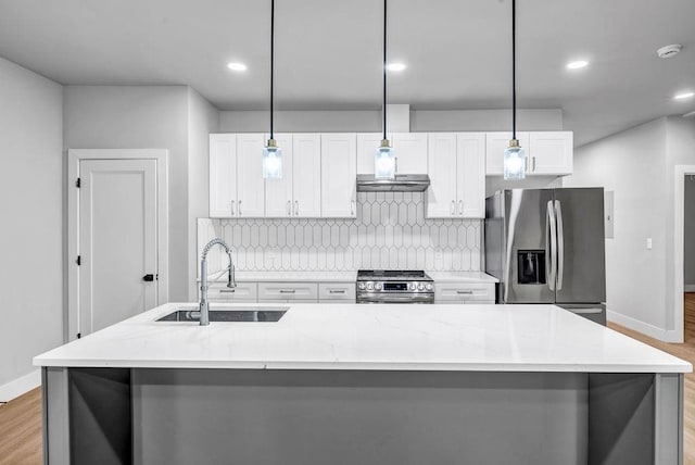 kitchen featuring stainless steel appliances, decorative light fixtures, and a center island with sink