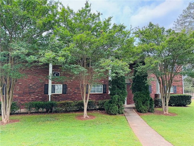 view of property hidden behind natural elements with brick siding and a front yard