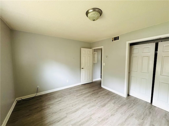 unfurnished bedroom featuring baseboards, visible vents, wood finished floors, and a closet