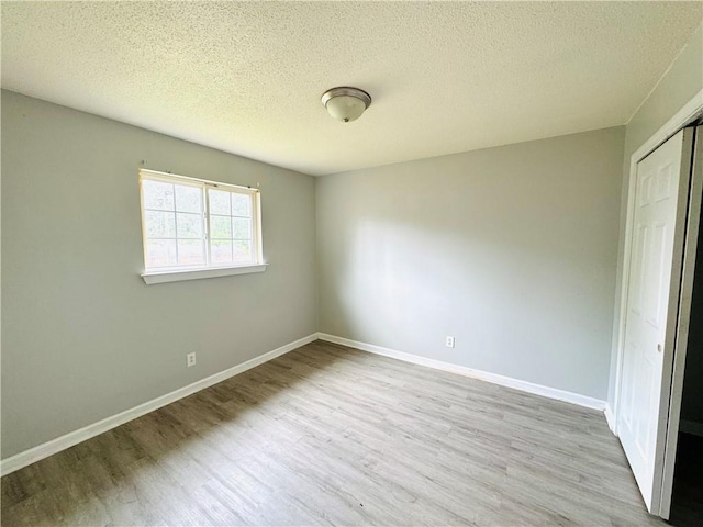 unfurnished bedroom with baseboards, a textured ceiling, wood finished floors, and a closet