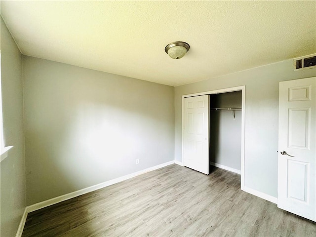 unfurnished bedroom with visible vents, a closet, wood finished floors, baseboards, and a textured ceiling
