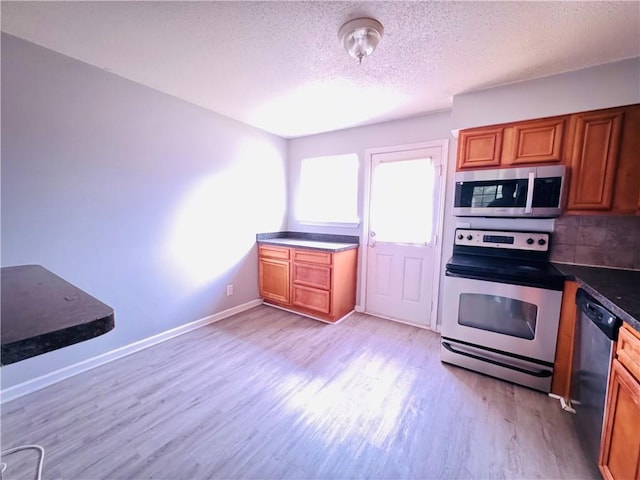 kitchen with baseboards, a textured ceiling, brown cabinets, light wood-style flooring, and stainless steel appliances