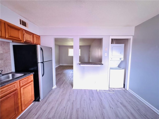 kitchen featuring brown cabinetry, stacked washer / dryer, visible vents, a sink, and freestanding refrigerator