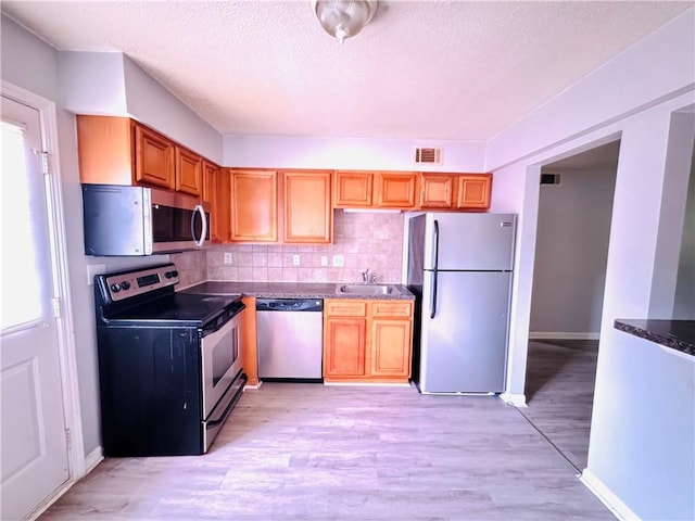 kitchen with visible vents, decorative backsplash, a sink, light wood-style flooring, and stainless steel appliances