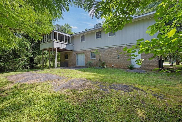 rear view of house featuring a lawn, a sunroom, and brick siding