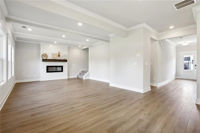 unfurnished living room with a large fireplace, visible vents, ornamental molding, wood finished floors, and beamed ceiling