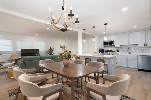 dining area with sink, an inviting chandelier, and light wood-type flooring