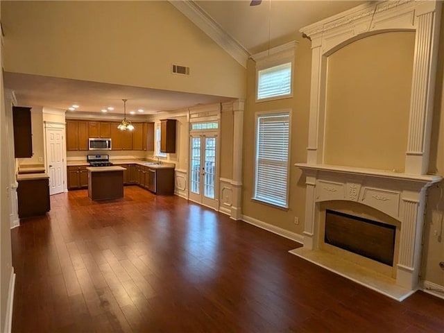 unfurnished living room with crown molding, a wealth of natural light, visible vents, dark wood-type flooring, and a glass covered fireplace