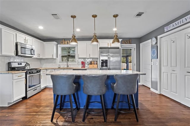 kitchen with visible vents, light stone counters, a kitchen island, white cabinetry, and stainless steel appliances