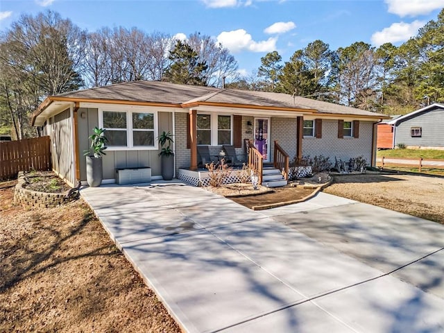 ranch-style home with board and batten siding, a porch, fence, and brick siding