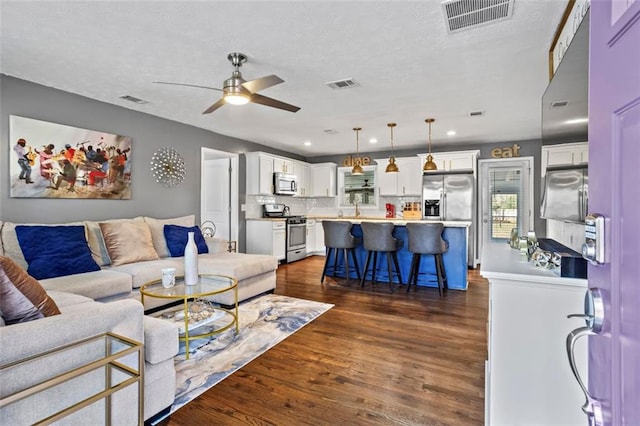 living area with a textured ceiling, dark wood-type flooring, visible vents, and ceiling fan