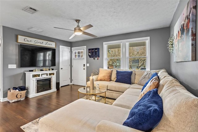 living area featuring wood finished floors, visible vents, a ceiling fan, a textured ceiling, and a glass covered fireplace