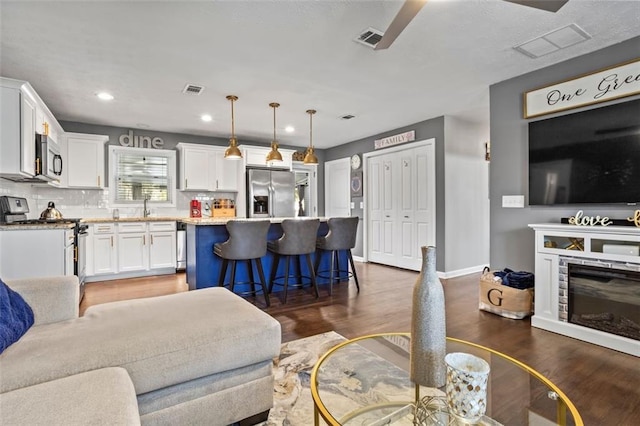 living room with a glass covered fireplace, visible vents, dark wood-type flooring, and baseboards