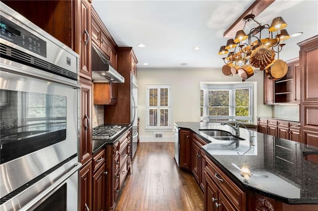 kitchen featuring appliances with stainless steel finishes, a notable chandelier, sink, an island with sink, and dark wood-type flooring