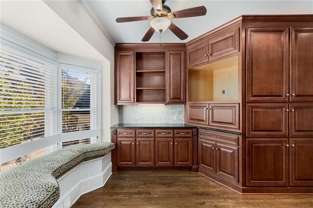 kitchen featuring dark stone countertops, ceiling fan, crown molding, dark wood-type flooring, and decorative backsplash