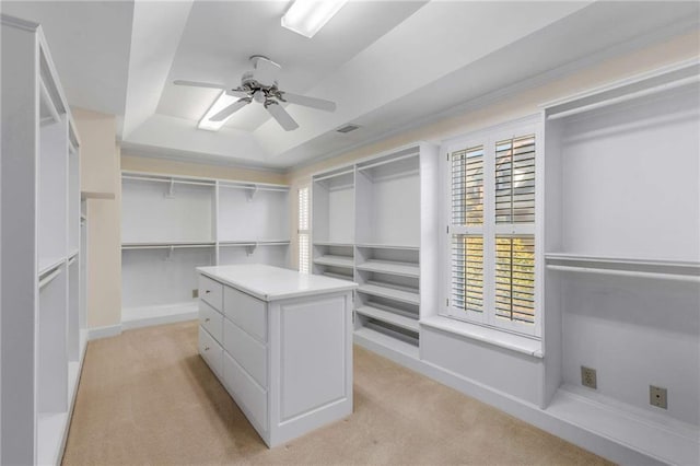 spacious closet featuring ceiling fan, light colored carpet, and a tray ceiling