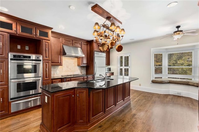 kitchen featuring appliances with stainless steel finishes, decorative backsplash, sink, an island with sink, and dark wood-type flooring