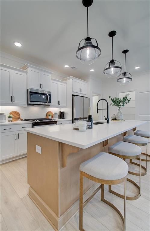 kitchen featuring an island with sink, white cabinetry, a sink, hanging light fixtures, and stainless steel appliances
