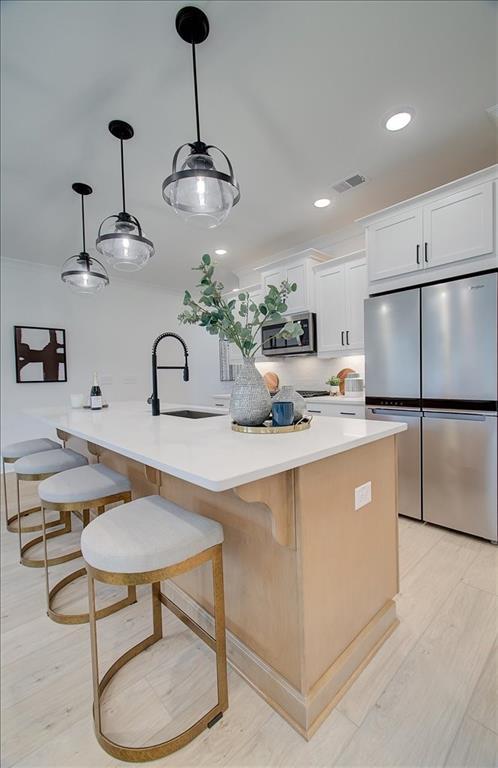 kitchen featuring pendant lighting, appliances with stainless steel finishes, a sink, a breakfast bar, and white cabinetry