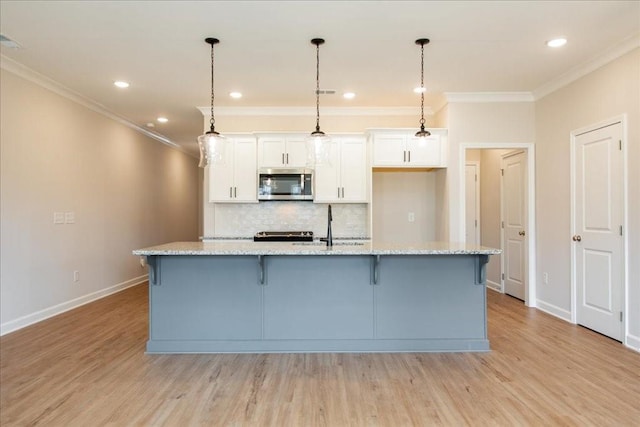kitchen featuring white cabinetry, stainless steel microwave, baseboards, light wood-type flooring, and ornamental molding