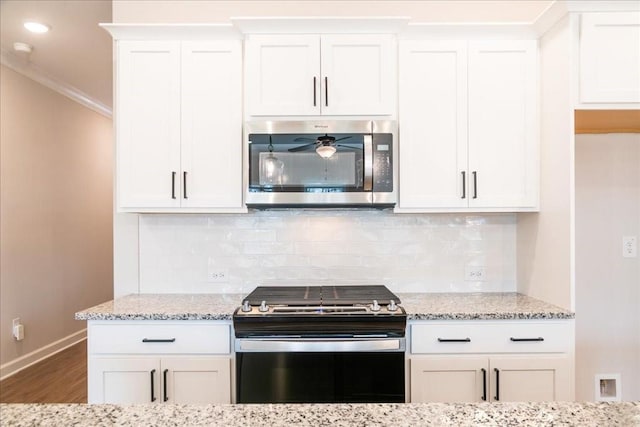 kitchen with wood finished floors, baseboards, white cabinets, stainless steel microwave, and gas range oven