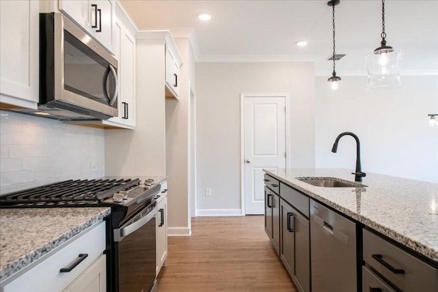 kitchen featuring backsplash, appliances with stainless steel finishes, a sink, light stone counters, and light wood-style flooring