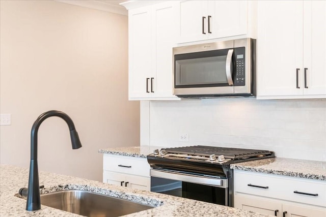 kitchen with appliances with stainless steel finishes, light stone counters, a sink, white cabinetry, and decorative backsplash