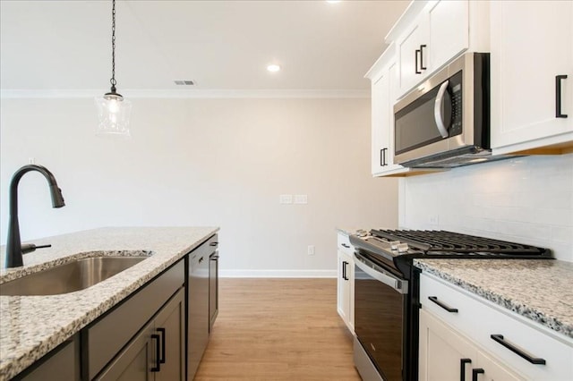 kitchen with appliances with stainless steel finishes, hanging light fixtures, a sink, baseboards, and ornamental molding