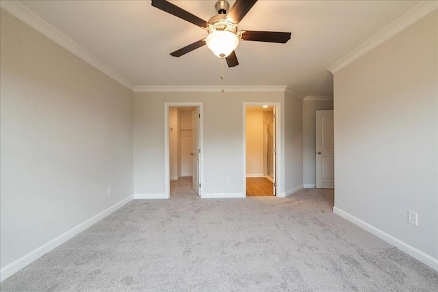 unfurnished bedroom with a ceiling fan, light colored carpet, crown molding, baseboards, and a spacious closet