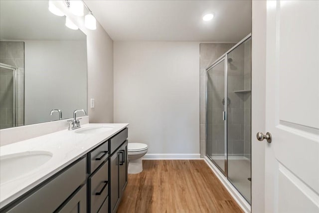 full bathroom with double vanity, a shower stall, wood finished floors, a sink, and toilet