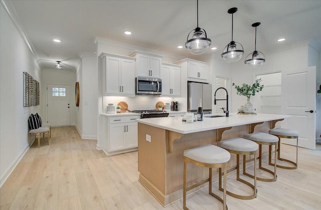kitchen featuring backsplash, appliances with stainless steel finishes, a center island with sink, a sink, and light countertops