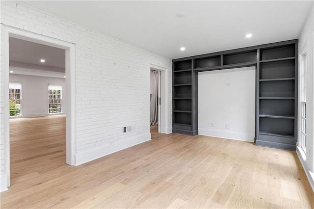 unfurnished bedroom with brick wall and light hardwood / wood-style floors