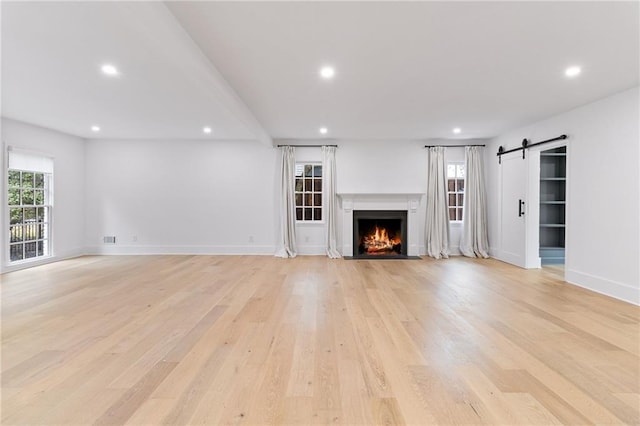 unfurnished living room with a barn door and light hardwood / wood-style floors