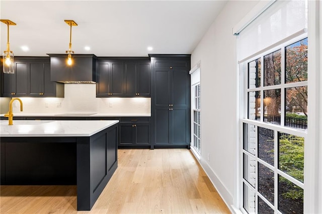 kitchen featuring sink, pendant lighting, wall chimney range hood, light hardwood / wood-style floors, and backsplash