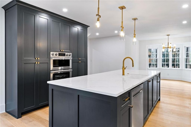 kitchen with sink, appliances with stainless steel finishes, hanging light fixtures, light hardwood / wood-style floors, and an island with sink