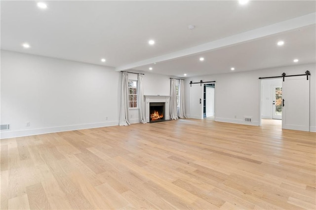 unfurnished living room featuring a barn door and light wood-type flooring