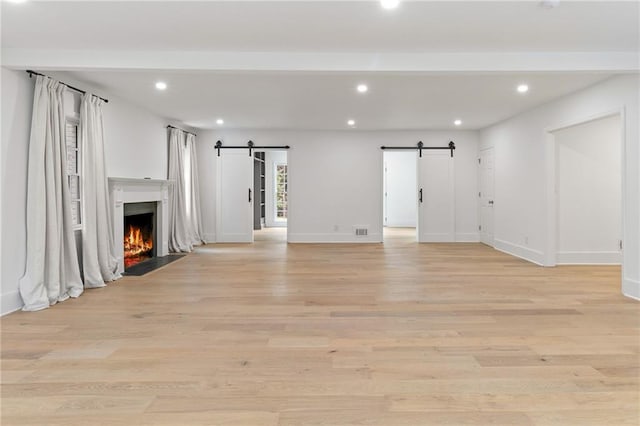 unfurnished living room with a barn door and light hardwood / wood-style flooring