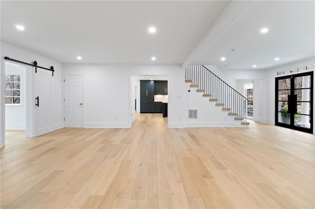 unfurnished living room featuring a barn door and light hardwood / wood-style flooring