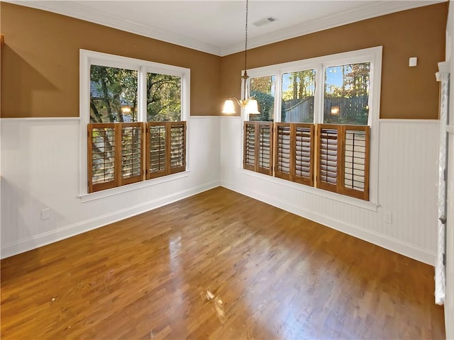 unfurnished dining area with hardwood / wood-style flooring, crown molding, and a notable chandelier