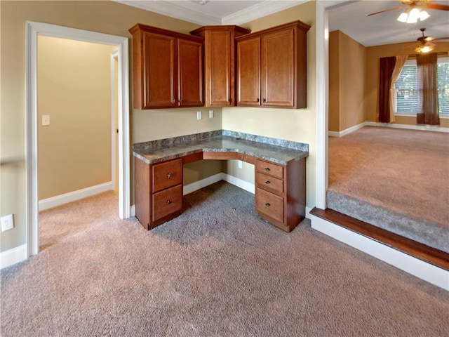 unfurnished office featuring built in desk, light colored carpet, ceiling fan, and crown molding