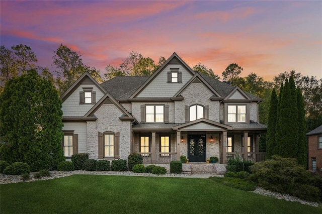 view of front of property featuring a porch, a lawn, and brick siding